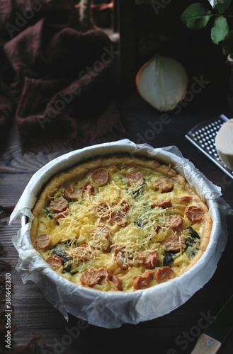 Quiche Lorraine, French tart made from pastry crust,milk, cheese, sausage and vegetables. Wooden textured background.