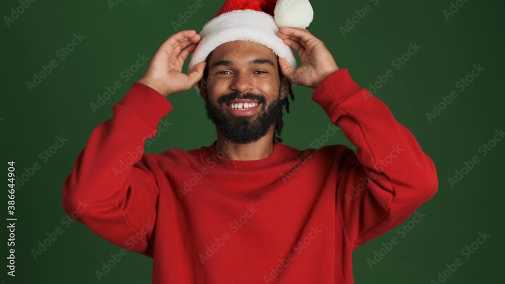Young happy african man in christmas santa hat isolated over green wall background Young happy african man in christmas santa hat isolated over green wall background