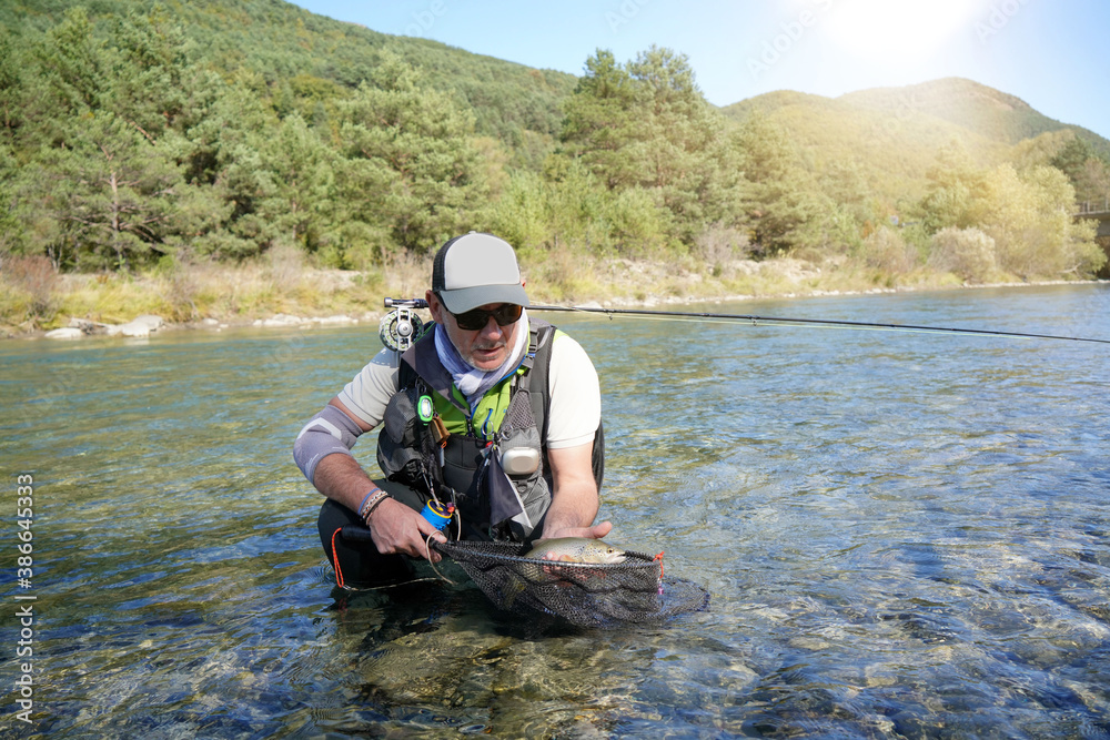 fly fisherman in summer catching a rainbow trout fishing in a mountain river fly fisherman in summer catching a rainbow trout fishing in a mountain river