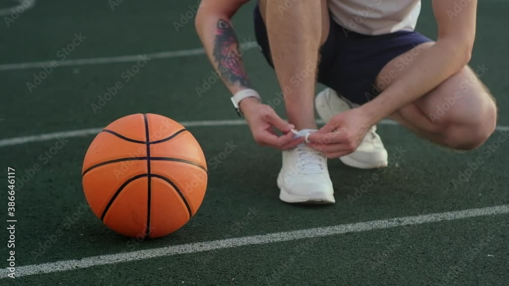 basketball player is tying lace on sporty shoes on court