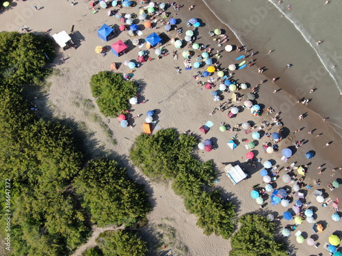 Vista cenital desde un dron, de la playa con arena, personas y sombrillas , un día de sol y calor.