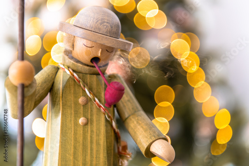 Räuchermann mit Stock, rauchend mit Pfeife, steht vor Weihnachtsbaum mit unscharfer Lichterkette photo