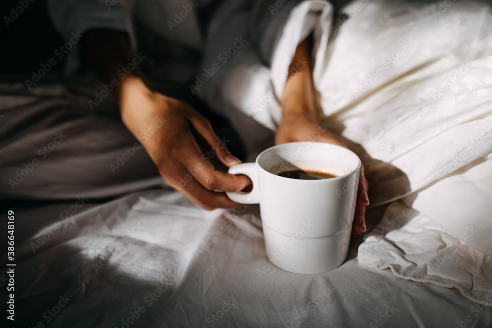Woman holding a cup of coffee, sitting on bed in the morning light. Woman holding a cup of coffee, sitting on bed in the morning light.