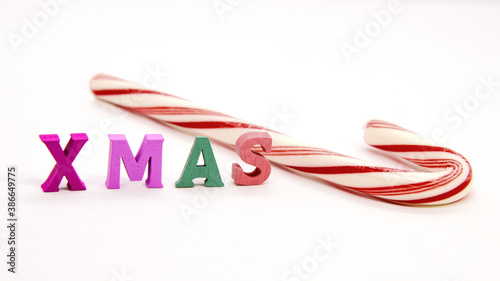 Word XMAS of colorful wooden letters and striped candy cane on white background. Christmas mood, gifts and preparation for holidays.