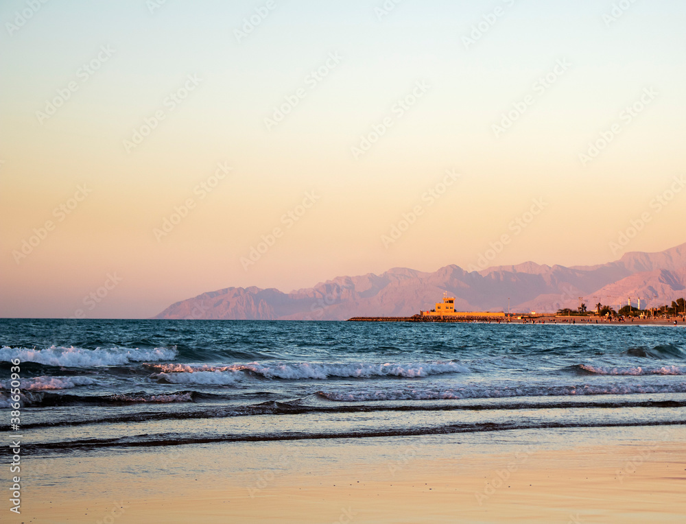 View of a waves on the beach and rocky shore during sunset. Shot taken in Ras Al Khaimah emirate. UAE.