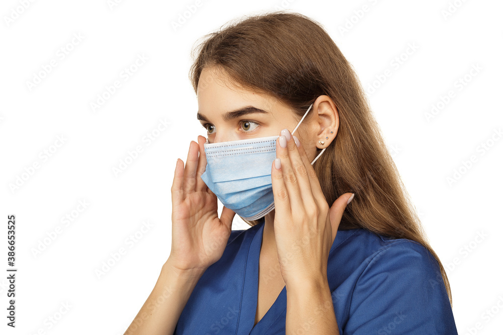 Beautiful young woman doctor surgeon putting on a protective disposable face mask isolated on white background. Virus protection concept. The modern viral threat of coronavirus Beautiful young woman doctor surgeon putting on a protective disposable face mask isolated on white background. Virus protection concept. The modern viral threat of coronavirus