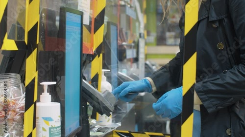 Woman in protective latex gloves paying by card at the checkout in a supermarket and picking up a purchase