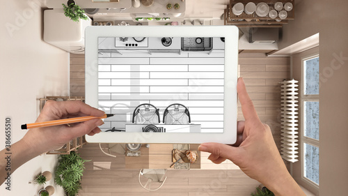 Hands holding and drawing on tablet showing wooden rustic kitchen details CAD sketch. Real finished interior in the background, architecture design presentation