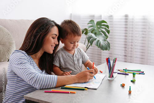 Young beautiful woman teaching her two year old son to draw at home. Woman spending quality time with her toddler child. Close up, copy space, background. photo