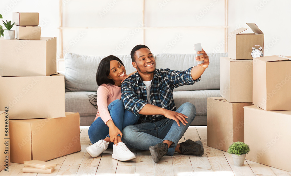 Smiling black guy and his girlfriend moving to their own home together, taking selfie among carton boxes, panorama Smiling black guy and his girlfriend moving to their own home together, taking selfie among carton boxes, panorama