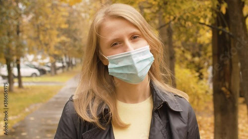 Portrait of young attractive woman in disposable mask against autumn park. Protection against a viral epidemic. Yellow leaves on the trees. Autumn day in the city