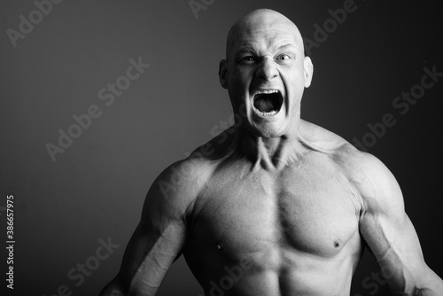 Bald muscular man shirtless against gray background