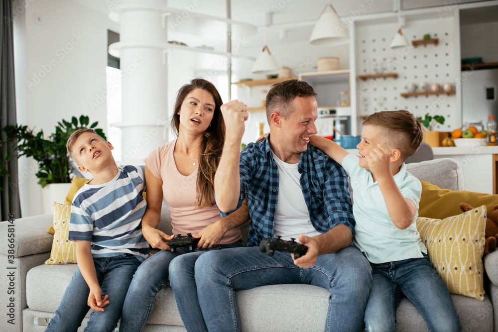 Husband and wife playing video games with joysticks in living room. Loving couple are playing video games with kids at home.