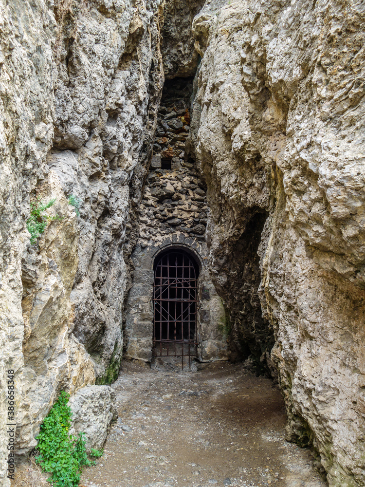 Artificial tunnel in mountain, which entrance covered by old iron grating. There's long cave behind it. This is last point of trekking route called Golitsin trail. Shot in Novyi Svit, Crimea