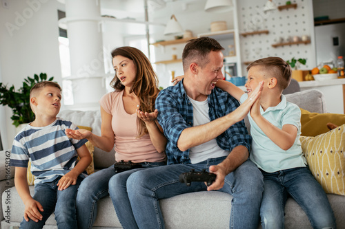 Husband and wife playing video games with joysticks in living room. Loving couple are playing video games with kids at home. photo