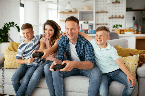 Husband and wife playing video games with joysticks in living room. Loving couple are playing video games with kids at home.