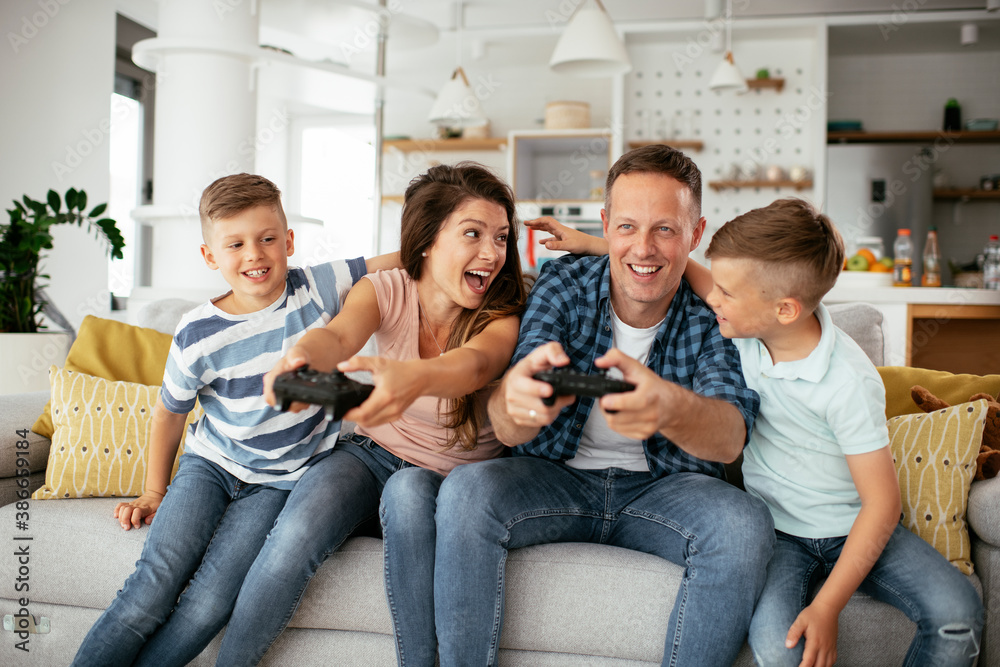 Husband and wife playing video games with joysticks in living room. Loving couple are playing video games with kids at home. Husband and wife playing video games with joysticks in living room. Loving couple are playing video games with kids at home.
