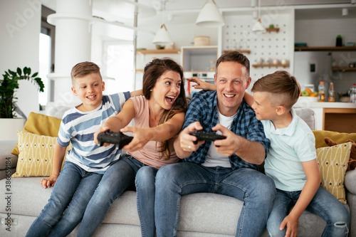 Husband and wife playing video games with joysticks in living room. Loving couple are playing video games with kids at home.