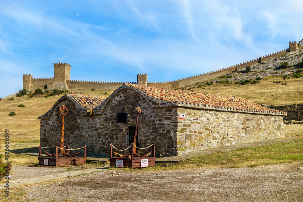 Medieval buildings for food storage inside of Genoese fortress, Sudak, Crimea. They built in XIV century. In front of them ancient anchors. Writings on plates translate as 'Museum piece. Don't touch'