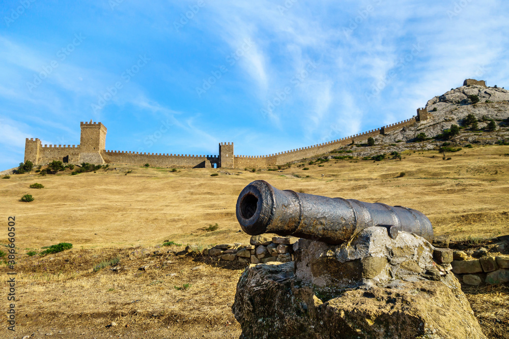 Cannon on a stone pedestal & medieval Genoese fortress on background, Sudak, Crimea. Also there are some stone remains of buildings, probably soldier barracks