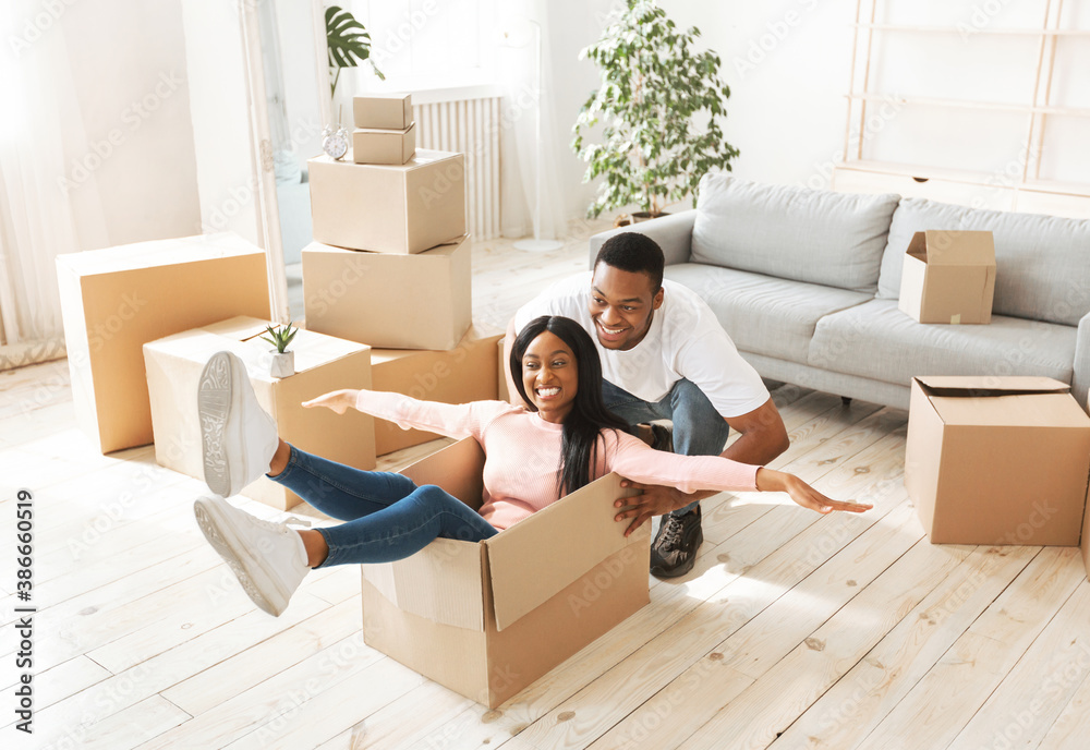 Beautiful black lady and her young husband playing together with cardboard box on moving day Beautiful black lady and her young husband playing together with cardboard box on moving day