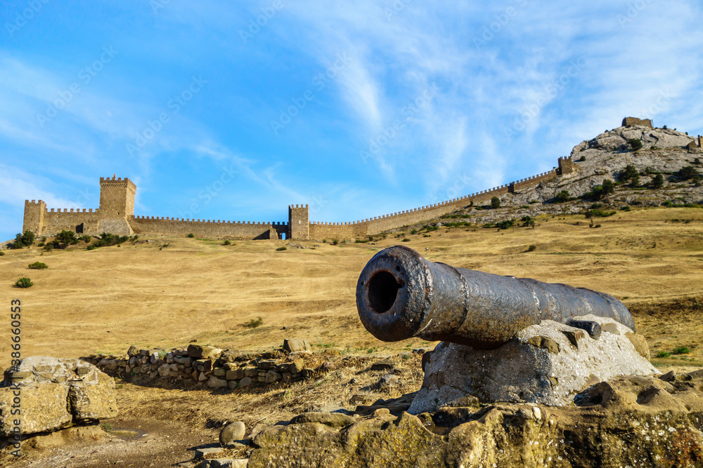 Cannon on pedestal of stone. Medieval Genoese fortress with its towers & walls on background. Shot in Sudak, Crimea