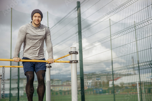 Young white man in his thirties is exercising in the street. A strong well built guy lifts the body behind the horizontal bar © Кирилл Горшков