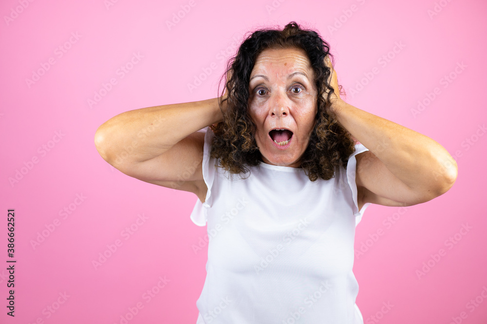 Middle age woman wearing casual white shirt standing over isolated pink background crazy and scared with hands on head, afraid and surprised of shock Middle age woman wearing casual white shirt standing over isolated pink background crazy and scared with hands on head, afraid and surprised of shock