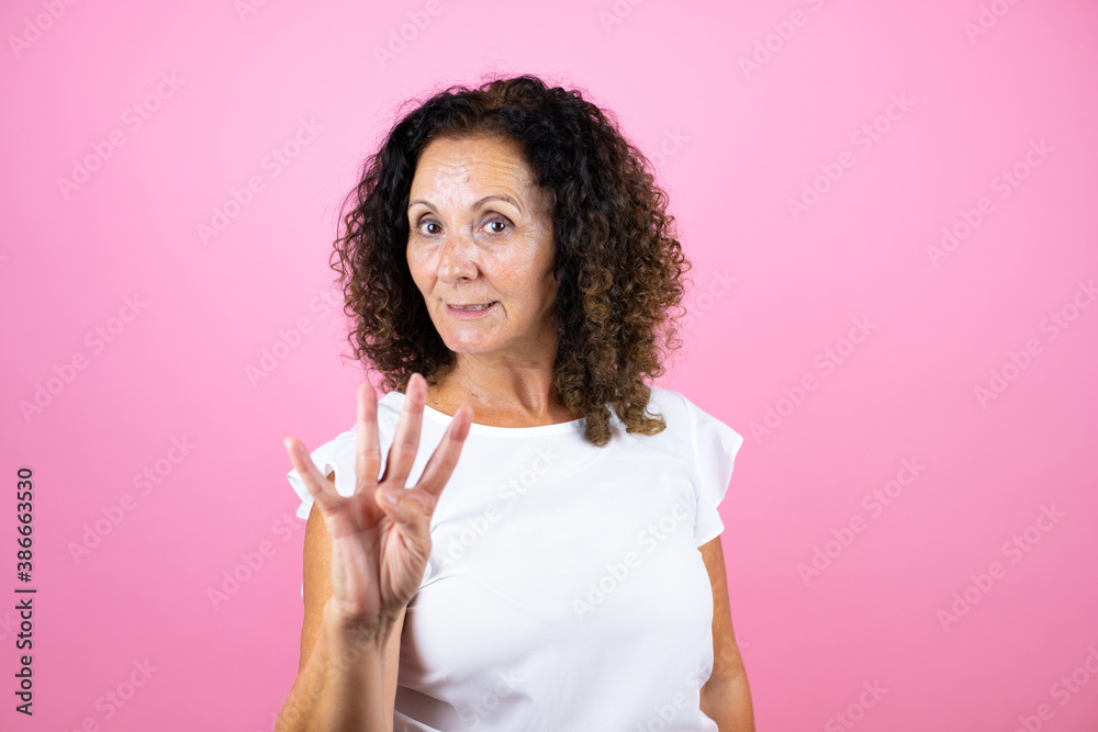Middle age woman wearing casual white shirt standing over isolated pink background showing and pointing up with fingers number four while smiling confident and happy