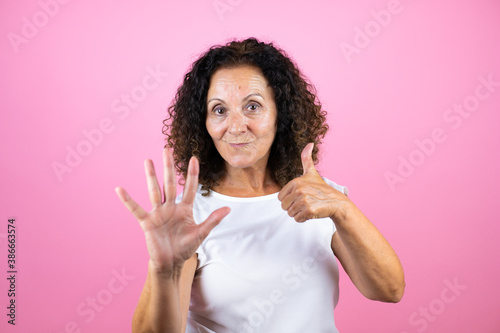 Middle age woman wearing casual white shirt standing over isolated pink background showing and pointing up with fingers number six while smiling confident and happy