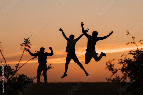 Silhouette of three Indian friends jumping with arms raised against the sky during the sunset 