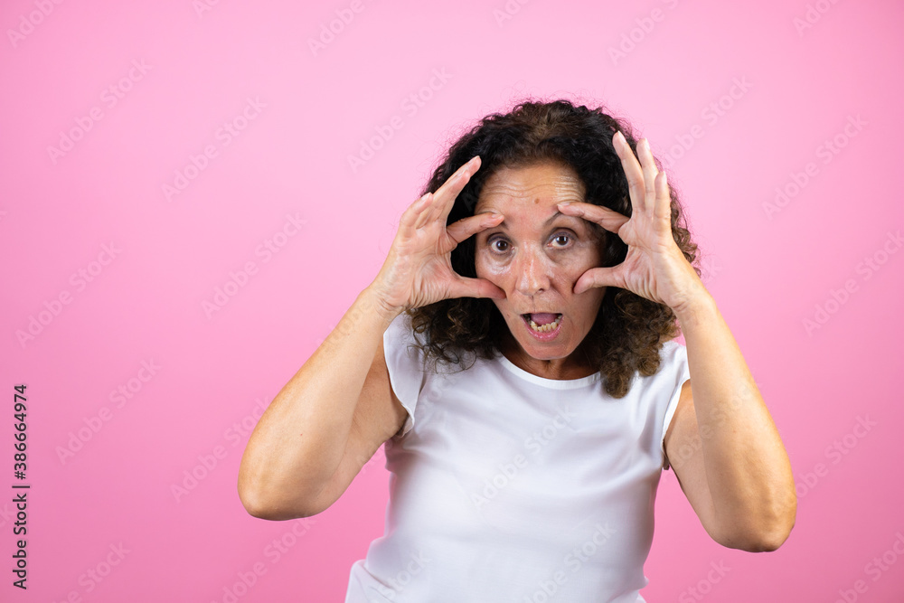 Middle age woman wearing casual white shirt standing over isolated pink background Trying to open eyes with fingers, sleepy and tired for morning fatigue