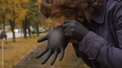 Close up man putting on black protective latex gloves against bokeh autumn city. Yellow leaves on the trees. Protection during viral epidemic. Blurry unrecognizable people walking along the street