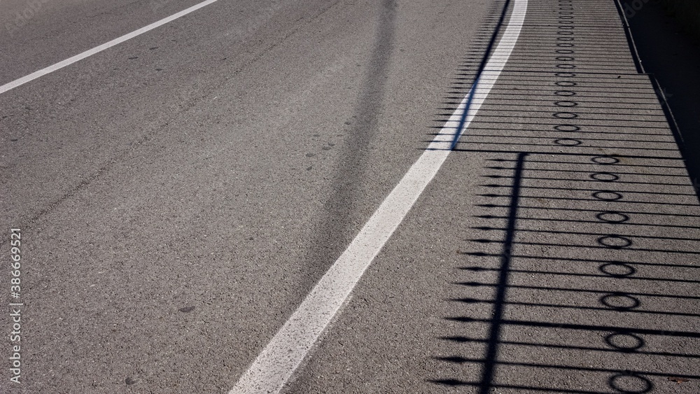 Fototapeta premium The shadow of a steel fence on the asphalt (Pesaro, Italy, Europe)