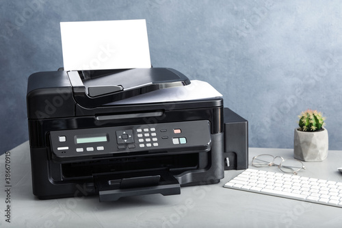 Modern printer with paper and computer keyboard on grey table