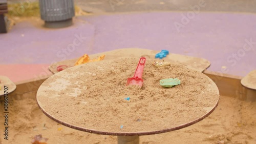 Close up forgotten kids toys in the sandbox. Rainy day. High angle view, steadicam shot