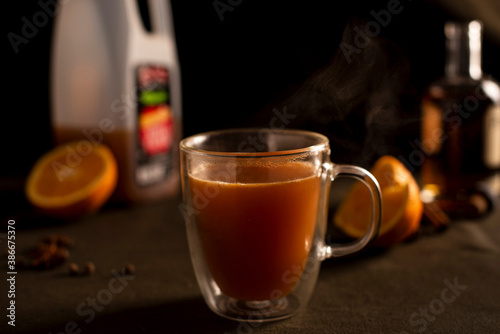 A mulled apple cider and orange cocktail with ingredients in background.