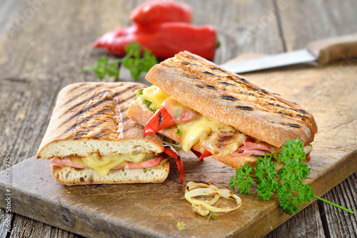 Getoastetes und im Kontaktgrill gepresstes italienisches Ciabatta mit Prosciutto, Käse und Grillgemüse  - Grilled Italian panini with ham, cheese and vegetables served on a wooden cutting board 