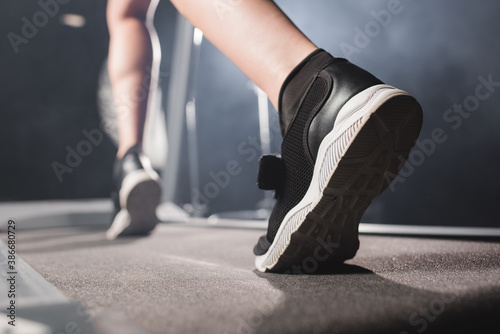 Selective focus of sportswoman in sneakers training on treadmill in gym