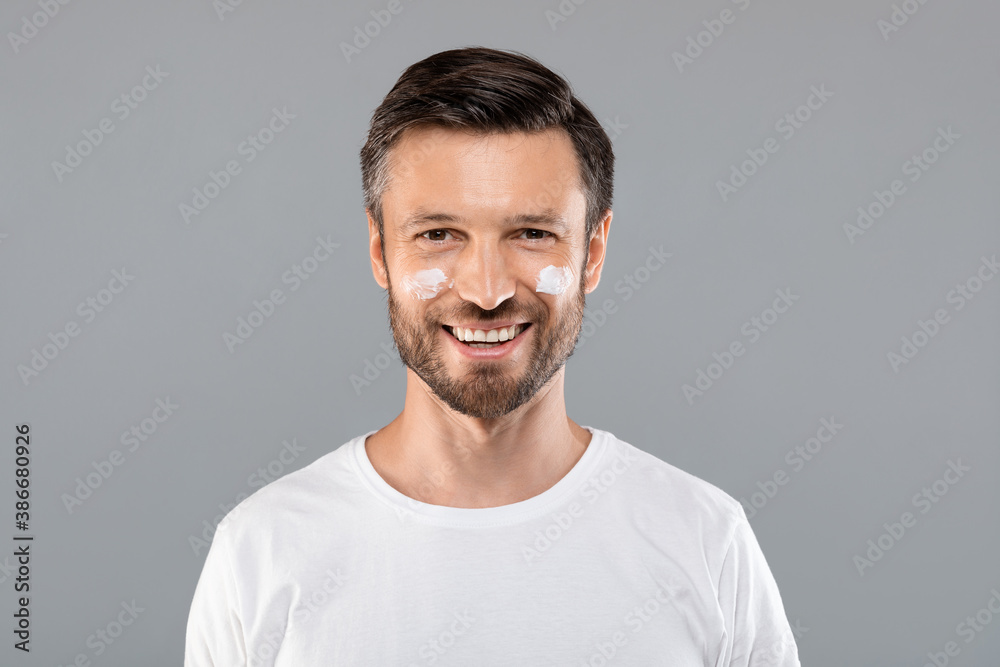 Middle-aged man with cream on cheeks against wrinkles