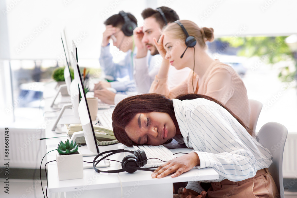 Fototapeta premium Tired hotline consultant sleeping at her desk, feeling exhausted or stressed after communication with customers