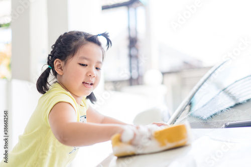 Car care with kid girl.6 years old asian child girl holding sponge with foam soap.washing car at home.Carwash service  Activity in family.Homeschool kid exercise.Lockdown during covid19 coronavirus.