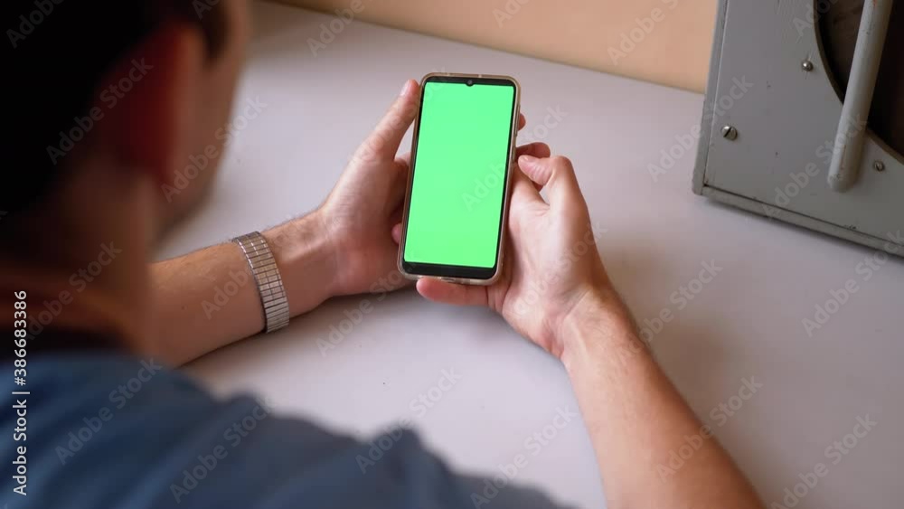 Man Holds a Smartphone with a Green Touchscreen on Table. Looking Display Man Holds a Smartphone with a Green Touchscreen on Table. Looking Display