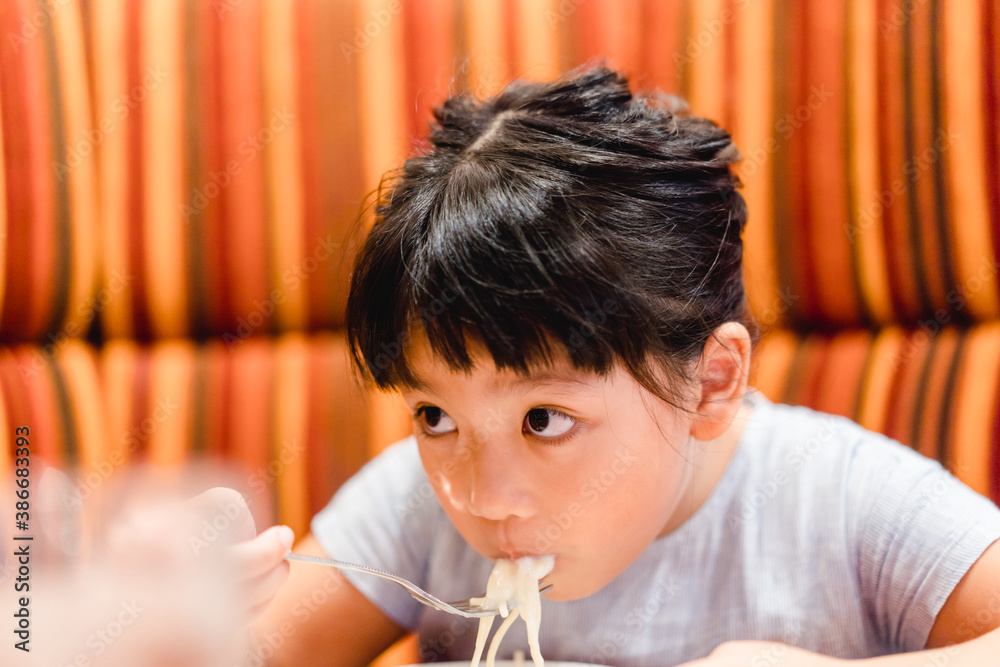 Hungry face and enjoy eating concept.Little asian girl enjoy eating with spaghetti carbonara with cheese on a plate in lunch time at restaurant.kid eating pasta.Delivery food, Delicious face. Hungry face and enjoy eating concept.Little asian girl enjoy eating with spaghetti carbonara with cheese on a plate in lunch time at restaurant.kid eating pasta.Delivery food, Delicious face.