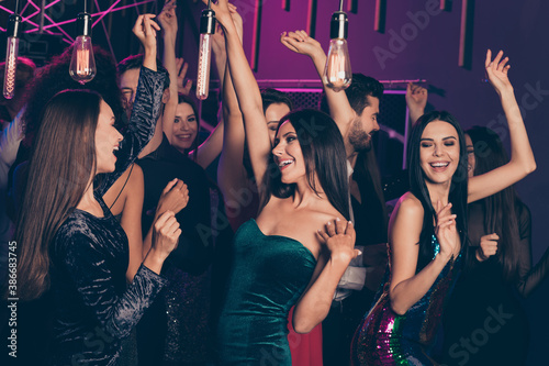 Photo of company celebrating prom at party in the night club dancing together laughing relaxing hands up wearing festive clothes