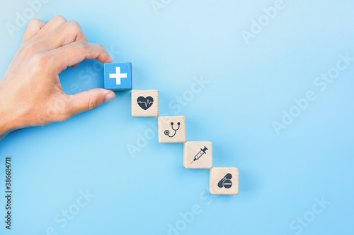 Health insurance concept, Hand holding wooden blocks with healthcare medical icons on blue background, copy space