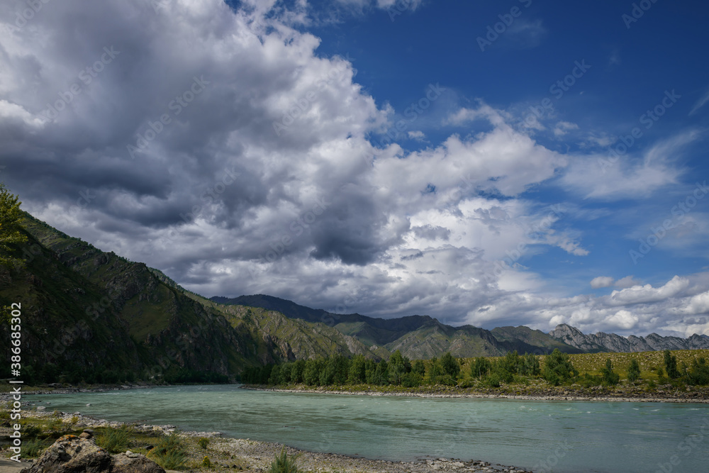 Majestic Katun river surrounded by rocky mountains, wooded banks against a blue sky with white clouds. Beautiful natural landscape.