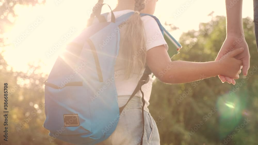 mom and daughter go to school. happy family education concept. schoolgirl with mom and daughter go hand in hand to lifestyle school on footpath in the park. little girl with a briefcase time to study