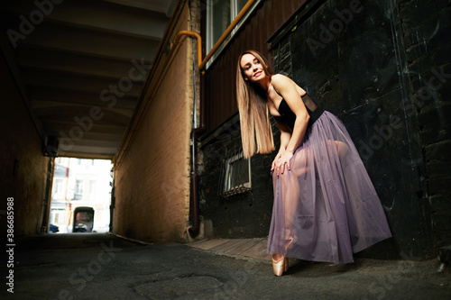 A beautiful adult woman with long hair standing on point shoes outdoors in city.