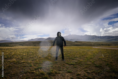 Strange man in black hood and gas mask on the background of mountains, around smoke, fog and radioactive fallout. Concept of environmental pollution, chemical disaster. Ecological catastrophe.